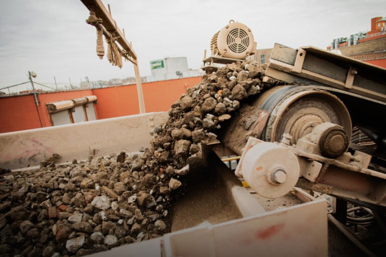A conveyor belt transporting and dropping a load of rocks and rubble into a container at an industrial or construction site.
